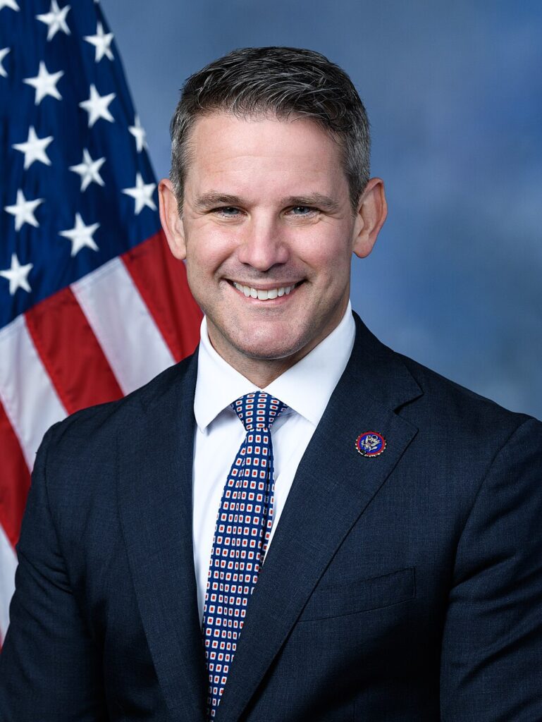 Photographic portrait on Adam Kinzinger against a flag of the United States of America